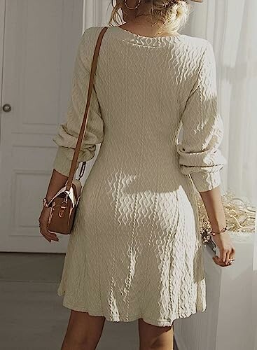 Woman in beige sweater dress with long sleeves and a small brown handbag.