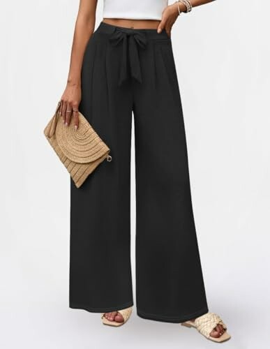 Woman wearing black wide-leg pants and holding a clutch