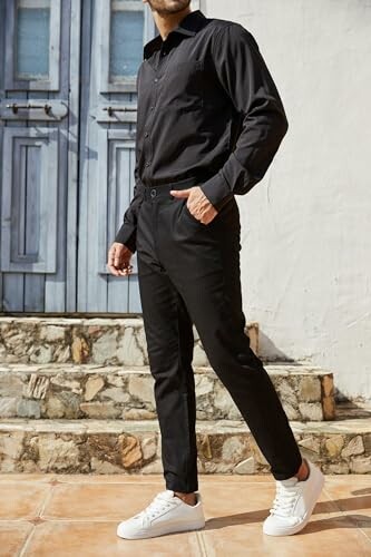 Man in black outfit with white sneakers standing on stone steps.