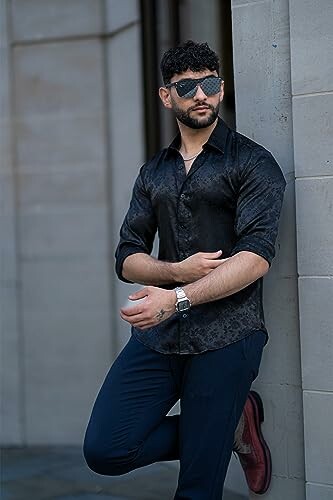 Man in sunglasses wearing a black shirt and leaning against a wall
