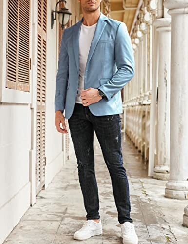 Man in blue blazer and jeans standing in a corridor.