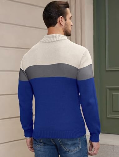 Man wearing a color-block sweater with blue, gray, and cream sections, viewed from the back.