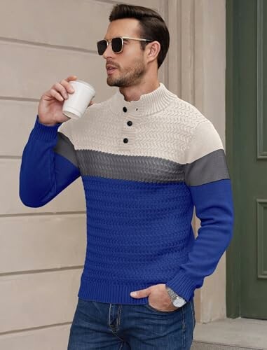 Man wearing a colorblock sweater with navy, gray, and cream sections, holding a coffee.
