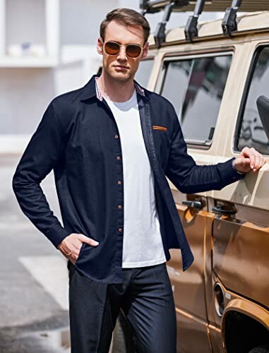 Man in sunglasses wearing a dark shirt and white t-shirt near a vehicle.