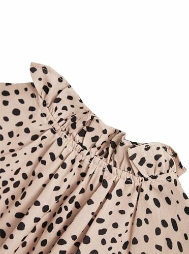 Close-up of a beige dress with black polka dots and ruffled neckline.