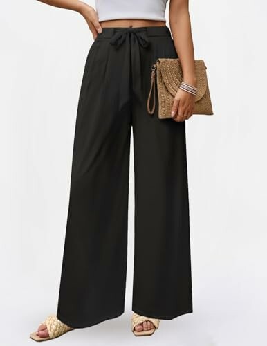 Person wearing wide-leg black pants and holding a woven clutch.