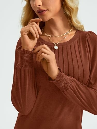 Woman wearing a brown blouse with pleated details and a necklace.