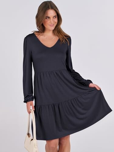 Woman in a black V-neck long-sleeve dress holding a white handbag.