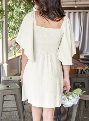 Woman in a light yellow dress holding white flowers indoors