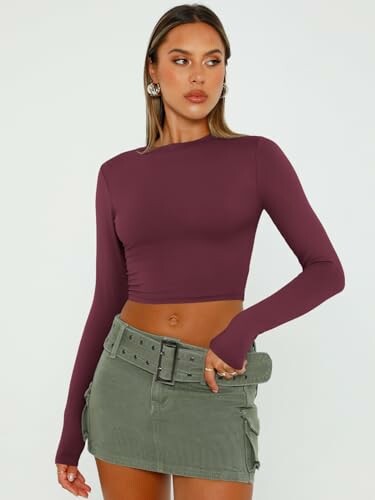 Woman in purple long-sleeve crop top and green skirt.