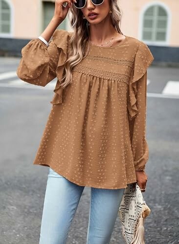 Woman in a brown blouse with ruffles and light jeans holding a bag.
