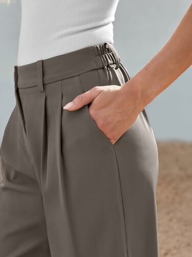 Close-up of a woman wearing gray pleated trousers with a hand in the pocket.