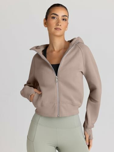 Woman wearing a beige zip-up hoodie and green leggings.