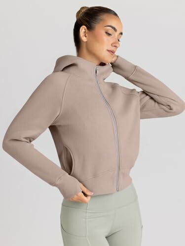 Woman in a beige hoodie with zipper and light green leggings.